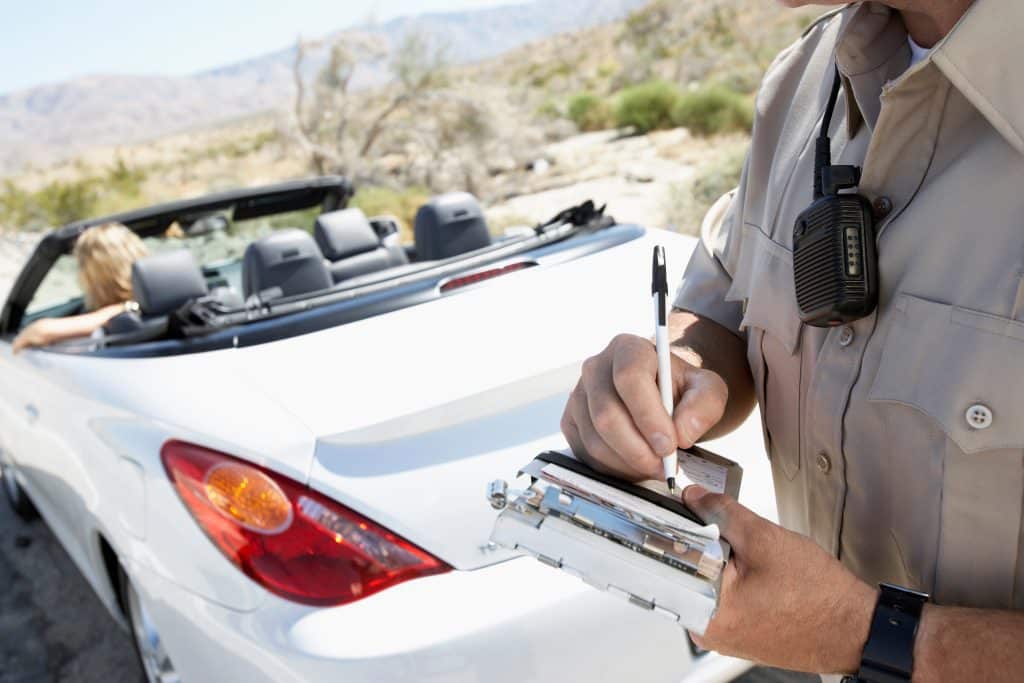 police officer writing a ticket behind a white convertible