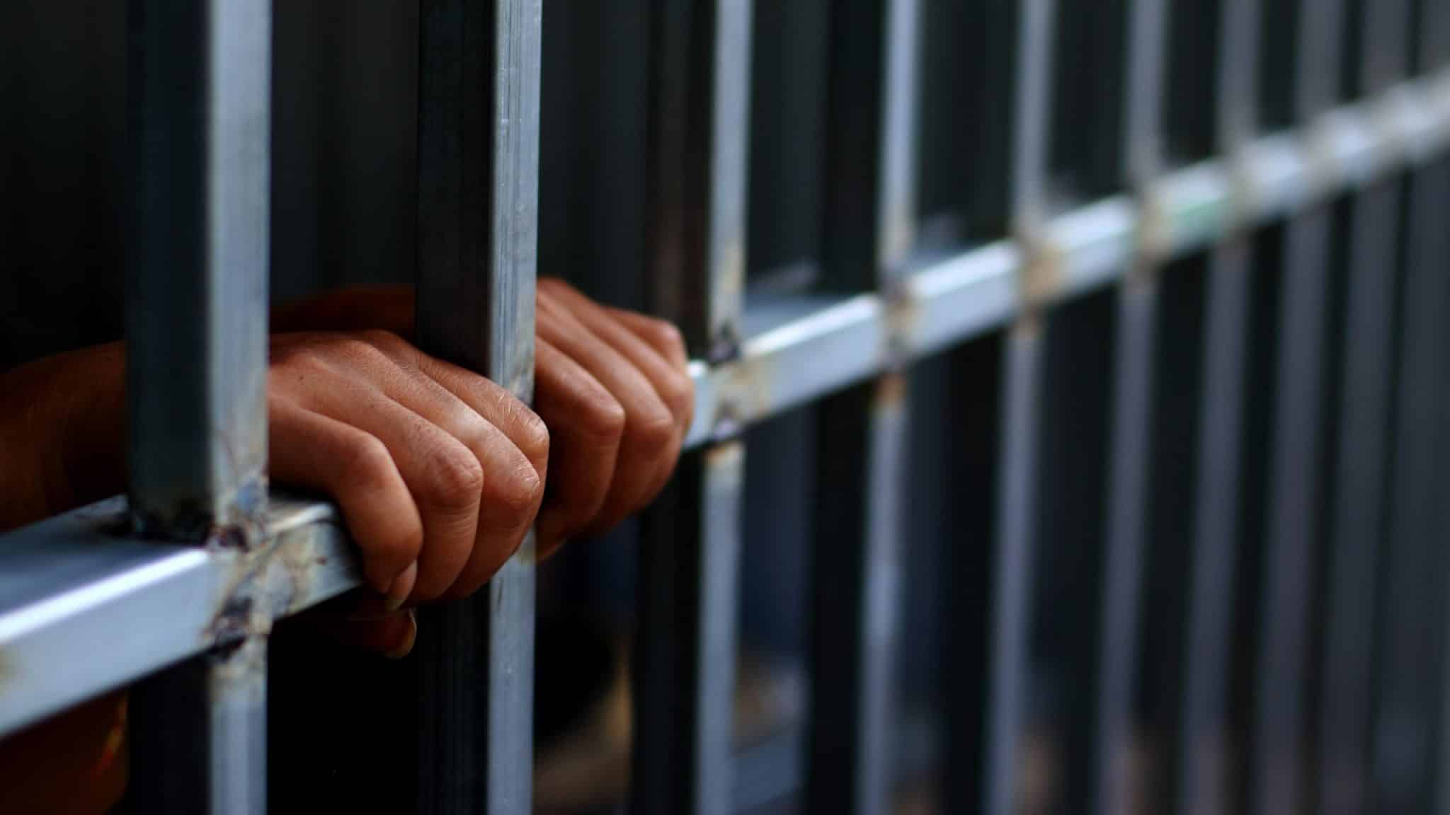hands resting on the bars of a jail cell