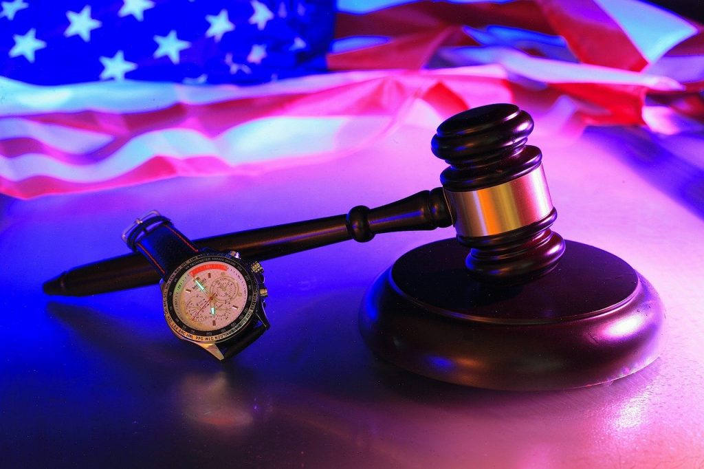 judge's gavel and a wrist watch set against an American flag background.