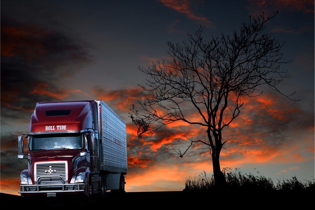red semi truck driving at dusk, near a tree