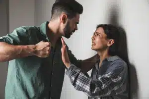 man holding his fist to a woman hepinned against the wall, who has a black eye