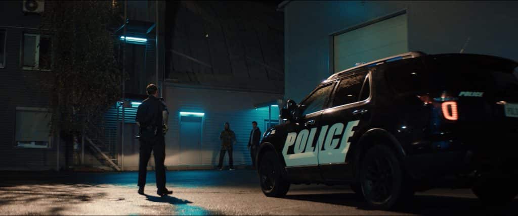 police officer standing next to police cruiser against a dark background